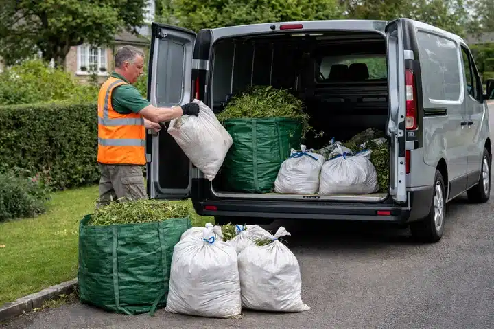 Garden waste collection van loading bagged debris on residential street.